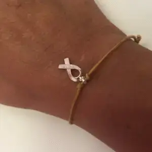 Team Jak's adjustable gold-toned Glow Gold Bracelet gold-toned cord bracelet features a delicate ribbon charm.