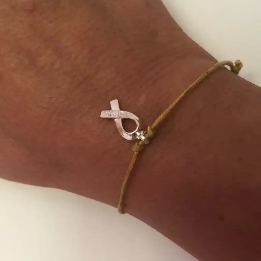 Team Jak's adjustable gold-toned Glow Gold Bracelet gold-toned cord bracelet features a delicate ribbon charm.